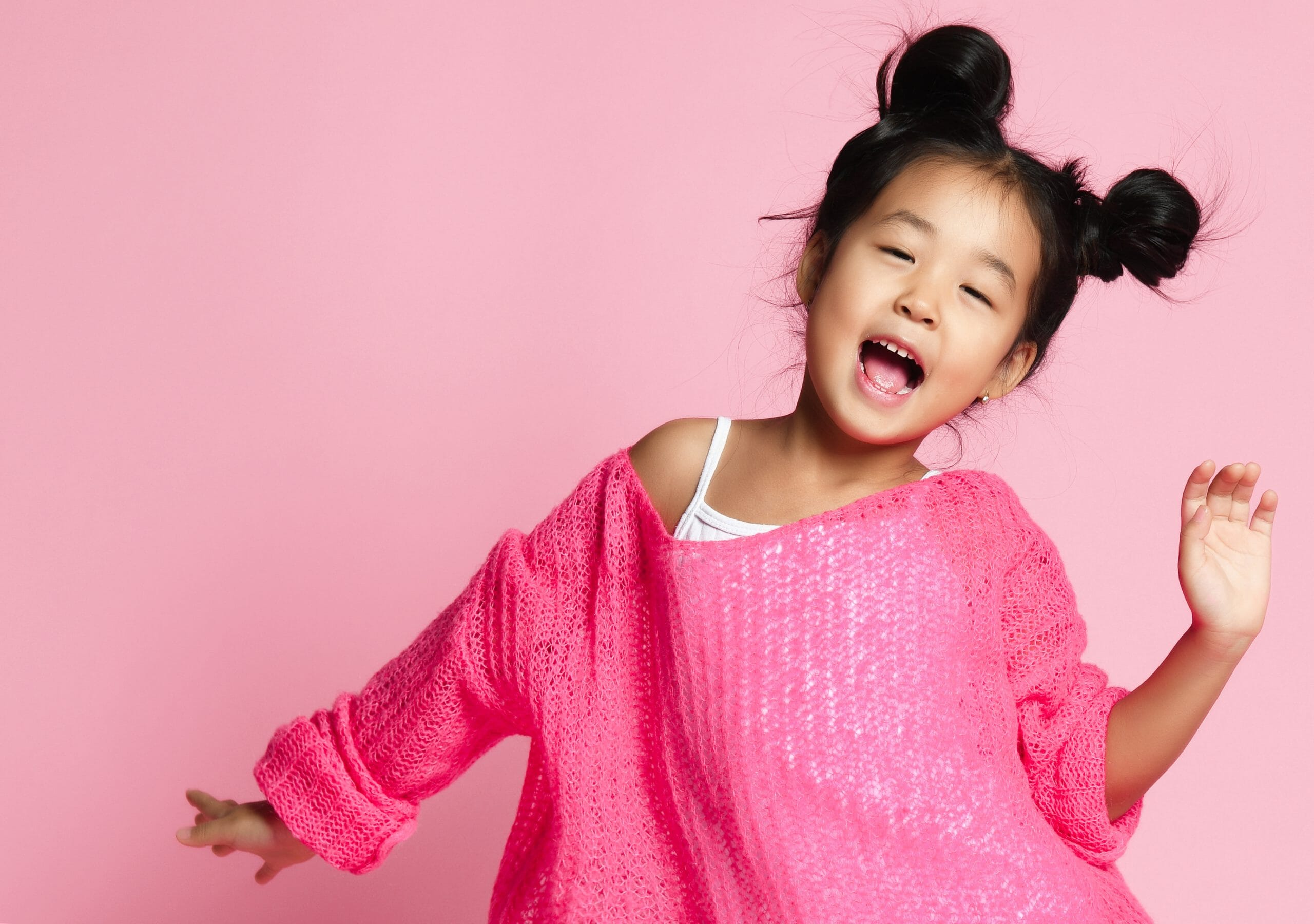 Asian kid girl in pink sweater, white pants and funny buns sings